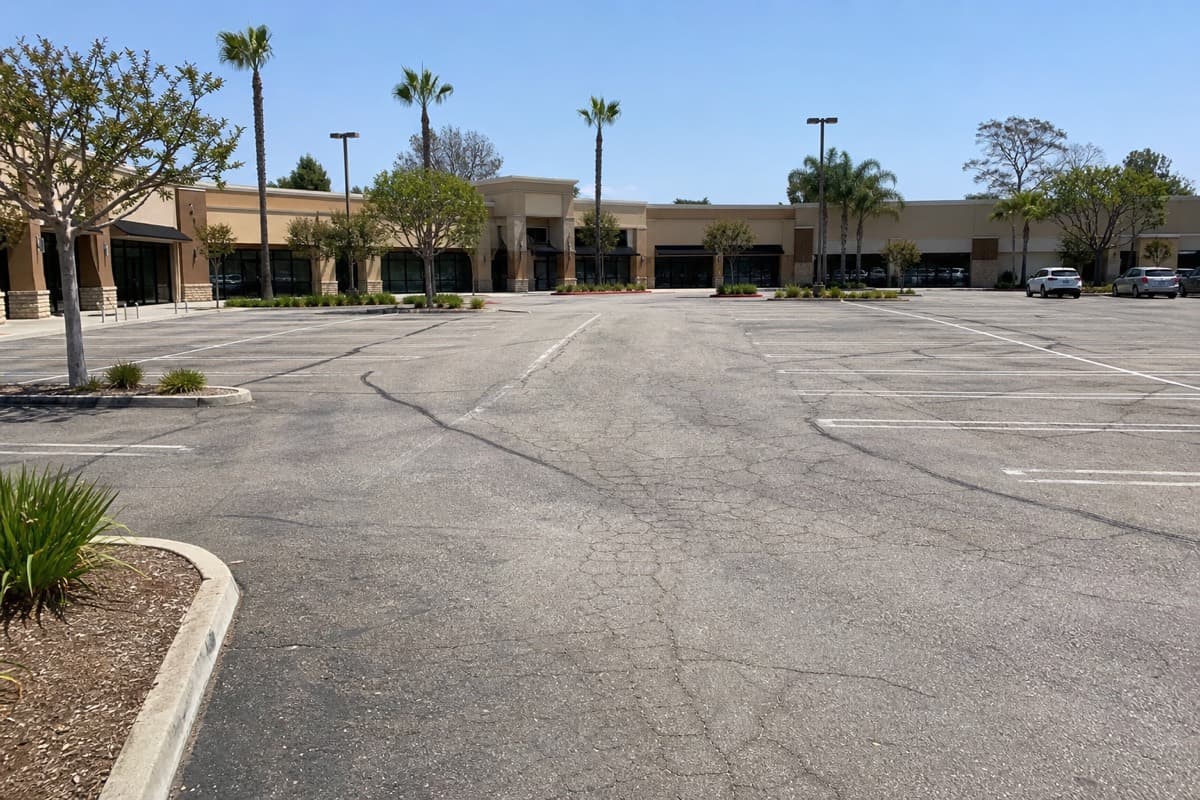 Full Southern California commercial parking lot with worn gray asphalt, cracks, patches, and faded striping before resurfacing